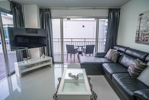 Modern living room interior with large sofa and flat-screen TV leading to a balcony