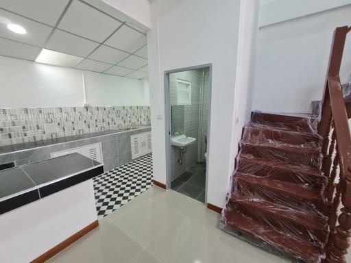 Modern staircase with wooden railing beside a kitchen and a bathroom with checkered tile flooring