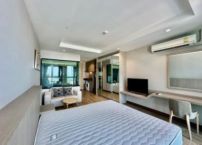 Modern bedroom with integrated living space, including a bed, couch, TV, and kitchenette