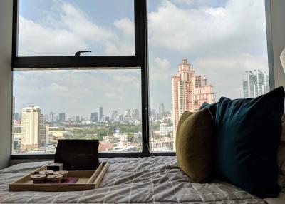 Cozy bedroom with a city view through a large window, featuring a comfortable bed and decorative pillows