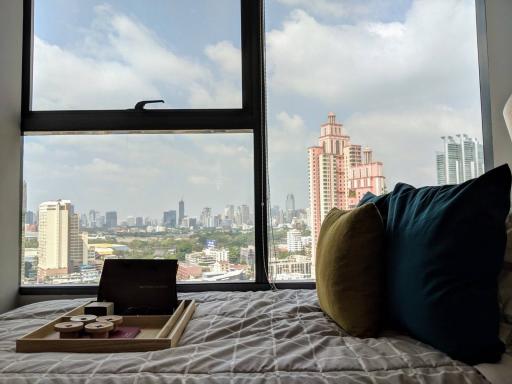 Cozy bedroom with a city view through a large window, featuring a comfortable bed and decorative pillows