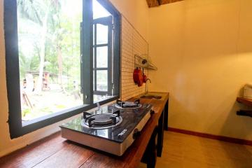 Compact kitchen with a gas stove, open window view, and tropical surroundings