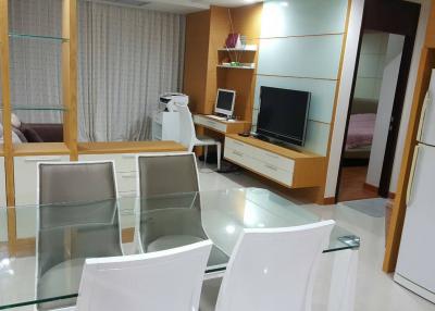 Modern living room with glass dining table, entertainment unit, and cream-colored decor