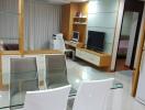 Modern living room with glass dining table, entertainment unit, and cream-colored decor