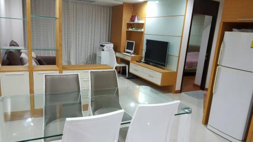 Modern living room with glass dining table, entertainment unit, and cream-colored decor