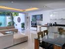 Modern open concept living room with kitchen, ample lighting, and glass dining table