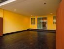 Spacious empty room with yellow walls, dark flooring and glass doors