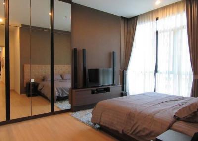 Modern bedroom with large bed, mirrored closet, and entertainment system