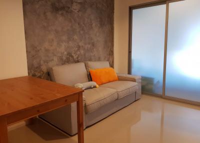 Modern living room with minimalist decor, featuring a gray sofa, textured wall, and large sliding glass door