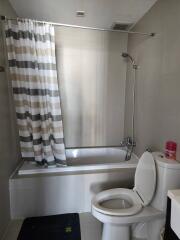 Modern bathroom with shower curtain, bathtub, toilet, and tiled flooring