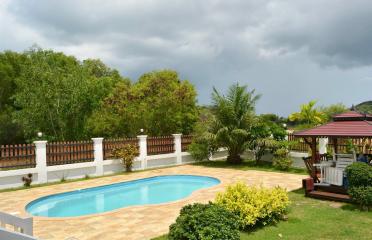 Spacious backyard with a swimming pool, gazebo, and greenery under a cloudy sky