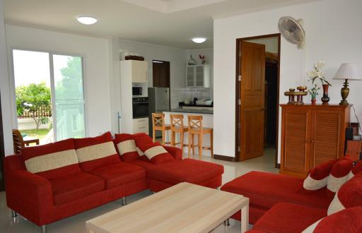 Spacious living room with red sofa, open kitchen, and balcony access