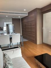 Modern kitchen with stainless steel appliances and wooden cabinetry adjacent to a living area with hardwood flooring