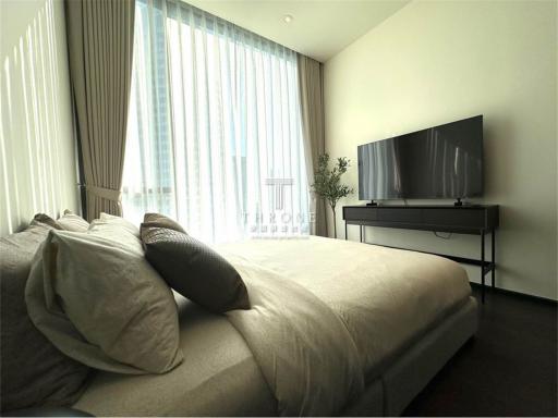 Modern bedroom with king-sized bed, large windows with curtains, and flat-screen TV