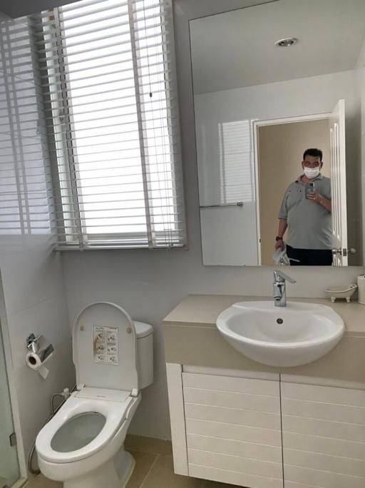 Modern bathroom with white fixtures, including a wall-mounted sink, toilet, and mirrored medicine cabinet, featuring venetian blinds on the window