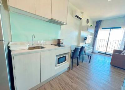 Modern apartment kitchen with dining area leading to a well-lit living room with balcony access