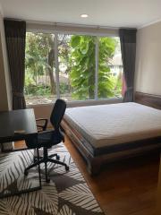 Bright bedroom with a large window overlooking greenery, featuring a study area and wooden flooring