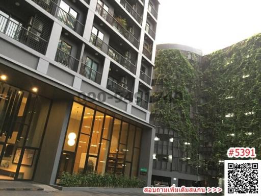 Modern residential building exterior with green climbing plants and a well-lit entrance