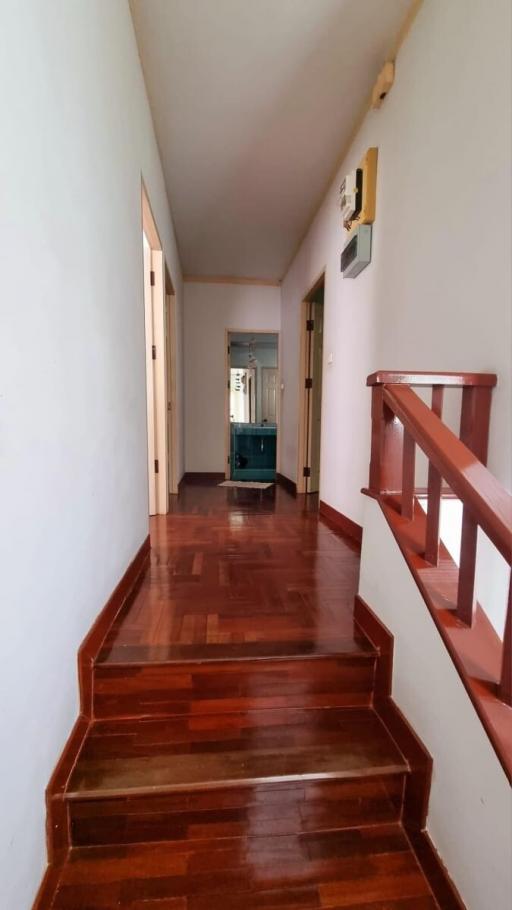 Warmly lit hallway with polished wooden stairs and flooring leading towards rooms