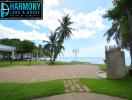 Paved pathway leading to a beachfront with clear skies and lush greenery