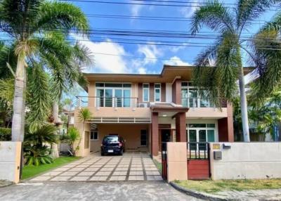 Modern two-story house with a car parked in the driveway, surrounded by tropical plants