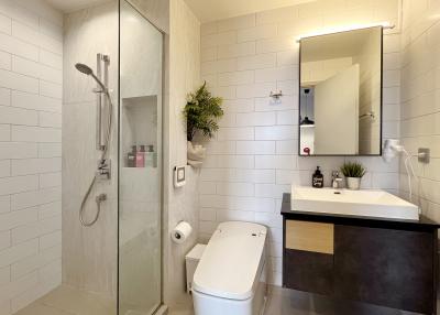 Modern bathroom with glass shower enclosure, white tiles, and plant decor