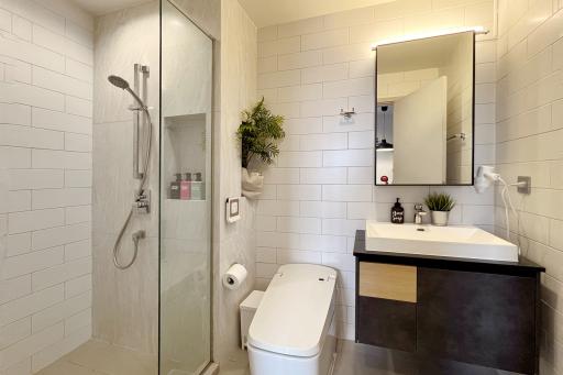 Modern bathroom with glass shower enclosure, white tiles, and plant decor