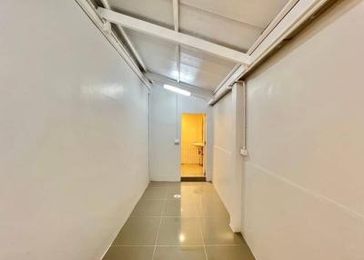 Narrow corridor with white walls and tiled floor leading to a brightly lit room