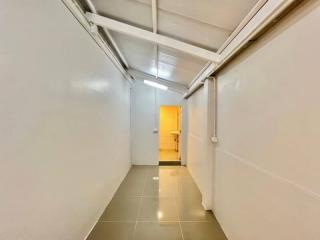 Narrow corridor with white walls and tiled floor leading to a brightly lit room