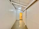 Narrow corridor with white walls and tiled floor leading to a brightly lit room