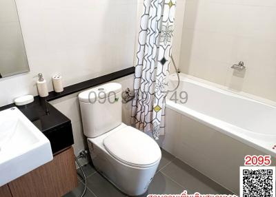 Modern bathroom with white fixtures, including a bathtub and sink, with partially visible shower curtain