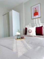 Cozy bedroom with a comfortable bed, decorative pillows, artwork on the wall, and a vase with flowers on the bedside table