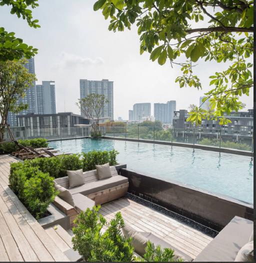 Modern outdoor swimming pool area with city skyline view, surrounded by greenery and a comfortable seating lounge