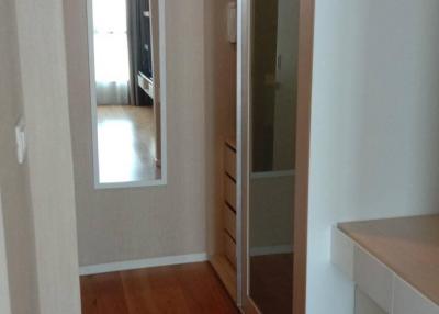 Narrow hallway with wooden flooring leading to a room with a glass door