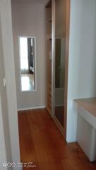 Narrow hallway with wooden flooring leading to a room with a glass door