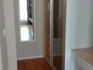 Narrow hallway with wooden flooring leading to a room with a glass door