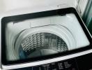 Top-loading washing machine in a small white utility space beside a window