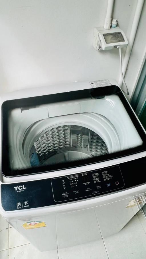 Top-loading washing machine in a small white utility space beside a window