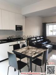 Modern kitchen with white cabinets and stainless steel appliances adjacent to living area with black leather sofa