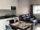 Modern kitchen with white cabinets and stainless steel appliances adjacent to living area with black leather sofa