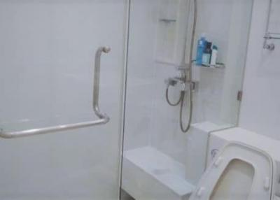 White tiled bathroom with shower, safety handrails, and modern fixtures