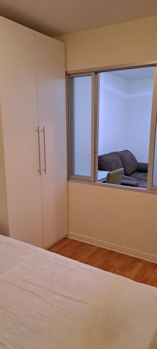 Cozy bedroom with wooden flooring and view into living area through window