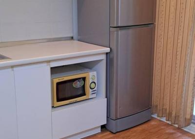 Compact kitchen with white cabinets, microwave, fridge, and hardwood flooring