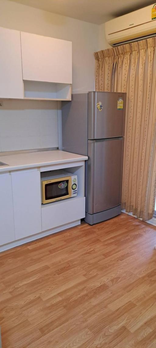 Compact kitchen with white cabinets, microwave, fridge, and hardwood flooring