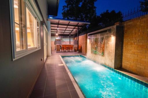 Cozy outdoor patio with illuminated swimming pool and dining area at dusk