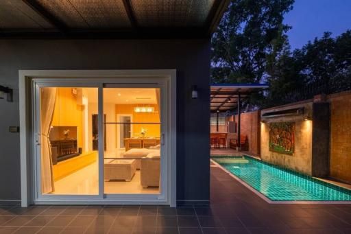 Modern home interior viewed from patio with sliding doors overlooking a swimming pool at dusk