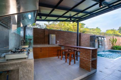 Spacious outdoor kitchen with modern appliances and adjacent dining area overlooking a pool and waterfall