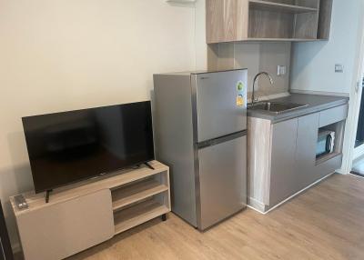 Modern studio apartment with integrated living area and kitchenette, featuring a flat-screen TV, refrigerator, and compact sink