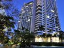 Modern high-rise residential building at dusk with exterior lighting and landscaping