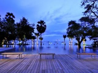 Elegant wooden deck overlooking a tranquil pool with palm trees and ocean view at dusk